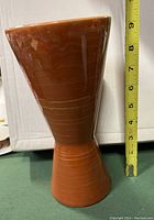 Side view of a glossy orange hourglass shaped ceramic vase approximately 9 inches tall
