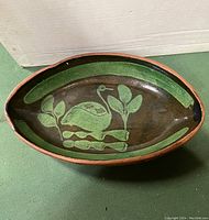 Oval pottery bowl with green swan motif inside and unglazed red edges.
