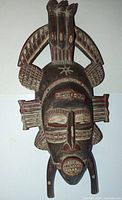 Front view of vintage African Senufo kpelie carved wooden mask, showing detailed handpainted patterns and three-dimensional crest and side decorations.