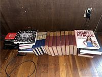 Books arranged on the floor in several rows, showcasing a mix of vintage hardcover volumes and modern books. Titles visible include various classic novels and nonfiction works.