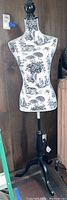 Front view of decorative dress form with black and white toile fabric and black wooden base.