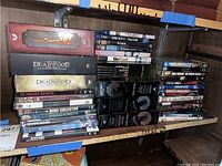 Shelf with DVDs featuring Indiana Jones boxed set, Deadwood complete seasons, James Bond movies, and others stacked horizontally and vertically.