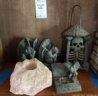 Front view of gargoyle bookends, skeleton lantern, pink mineral rock candle holder, and composite gargoyle candle holder on a wooden shelf