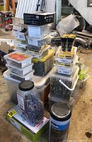 Stack of clear plastic containers and boxes with hardware including screws, washers, and fasteners.