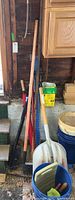 Lawn rake, measuring stick, branch trimmers and other garden tools leaning against shed wall with corner of blue bucket visible