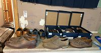 Multiple pairs of men's dress shoes on a table including wingtip and plain styles in various shades of brown and tan.