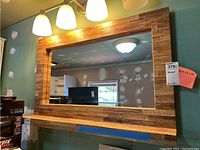 Front view of large rectangular wall mirror with integrated shelf and wood-like appliqué finish on frame and shelf.