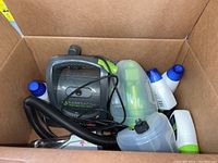 Photo of the BarkBath Qt portable dog bath system with shampoo bottles inside a cardboard box, showing the main unit, hose, and various bottles.