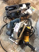 Photo showing Bosch circular saw, Stanley stapler with box of staples, and Dewalt angle grinder all together with cords and cases.