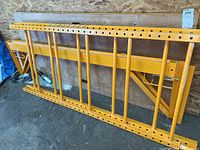 Two yellow powder-coated steel scaffold frame sections leaning against plywood wall