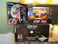 Four Star Trek items: dinnerware set box, Child's flatware box, talking alarm clock box, and 1994 edition signature series telephone box.