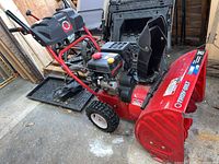 Full side view of red Troy-Bilt Storm 2410 snow blower showing auger housing, wheels, engine and controls.
