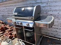 Full view of Weber Genesis gas grill showing front, control knobs, side shelves, and part of propane tanks attached below.