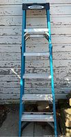 Full view of blue Werner 6-foot step ladder against an outdoor wall, showing all steps and top platform.