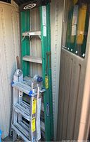 Photo showing both Werner ladders stored in a shed; 6ft green fiberglass step ladder and folded 13ft aluminum ladder.