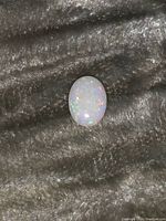 Oval white opal cabochon showing play of color against a dark textured background.