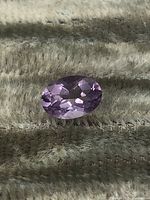 Close-up image of oval faceted amethyst gemstone showing purple color and faceting details.