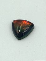 Top view of a triangular cabochon ammolite showing red and orange iridescent colors with a polished surface on a white background.