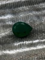 Top view of green pear-shaped emerald gem showing faceted surface and deep green color.