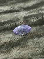 Close-up of the purple marquise-cut gemstone showing the cut, color, and facets on a textured fabric background.