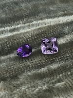 Two amethyst gemstones placed on green textured fabric, showing different purple shades and cuts.