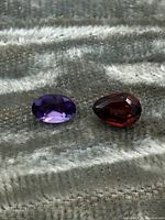 Both gemstones shown side by side on a textured gray fabric background highlighting their shape, cut and color.