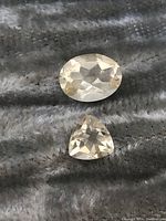 Two Madagascar citrine gemstones on textured gray fabric, one oval cut and one trillion cut, showing top facets and color.
