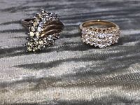 Front angled view of two vintage costume rings on fabric surface showing rhinestone details and gold-tone metal.