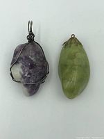 Two stone pendants: one amethyst wrapped in wire, one green stone with metal cap