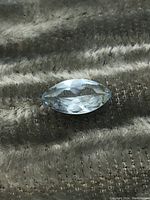 Close-up photo of the marquise cut blue spinel gemstone placed on a textured surface showing facets and color.