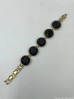 Full view of black stone bracelet, showing linked round faceted stones and gold-tone metal chain ends.