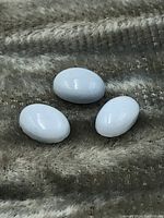 Top view of three oval blue opal cabochon gemstones placed on a textured fabric surface, showing their size and glossy finish.