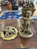 Brass figurine of two children climbing a wall and brass elephant door or fireplace hanger on a wooden surface in an indoor setting