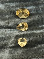 Three citrine gemstones shown individually in a close-up on a gray textured fabric to highlight color and faceting.