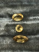 Photo showing three citrine gemstones arranged vertically on a textile surface, highlighting their shapes and color.