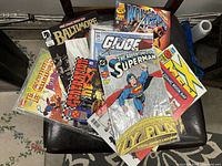 Top view of 16 vintage comic books fanned out showing covers featuring Superman, GI Joe, Wolverine, and others.