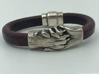 Front view of dark brown leather bracelet with silver-tone hand and paw clasp showing detailed texture on the clasp and magnetic closure