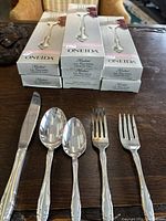 Boxes of Oneida Affection 5-piece place settings displayed behind each corresponding piece of flatware: knife, dinner spoon, teaspoon, dinner fork, salad fork.