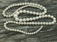 Pearl necklace laid out on dark textured fabric showing size gradation and absence of clasp.
