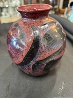 Photo of the front and side of the pottery vase showing its reddish glaze with black abstract patterns