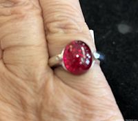 Ring worn on finger showing the ruby cabochon stone and silver band in natural lighting.