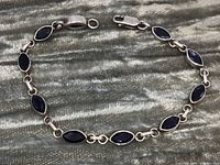 Full view of the sterling silver tennis bracelet laid flat showing the linked marquise blue stones and silver links