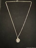 Full view of the necklace showing the entire silver chain and round pendant on a black background.