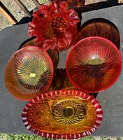 Overview of four pieces of hobnail sunset tinted glass: two round bowls with radiating line patterns, one ruffled hobnail bowl, and one elongated dish with a ruffled edge and pressed patterns.