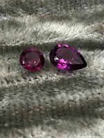 Two faceted tourmaline gemstones on a grey textured background, showing one round and one pear shape stone.