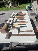 Overview of all 21 assorted hammers laid out on a white folding table outside showing various styles including mallets, claw hammers, sledgehammers, and specialty hammers with wooden and composite handles.