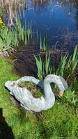 Concrete goose garden statue positioned on grass by pond, showing side profile and surface condition with paint scuffs and weathering.