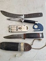 Lot items arranged for overview: fixed blade dagger, Japanese switchblade folding knife, metal paint scraper cutter, and blue plastic scraper tool.