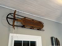 Full side view of the wooden Fleetwing Racer snow sled showing the metal frame and wooden slats with painted logo.