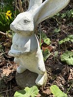Front side view of the white concrete hare sculpture among garden plants and soil, showing overall form and size